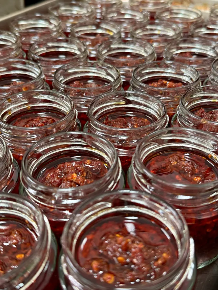 Rows of chilli oil jars being filled by hand