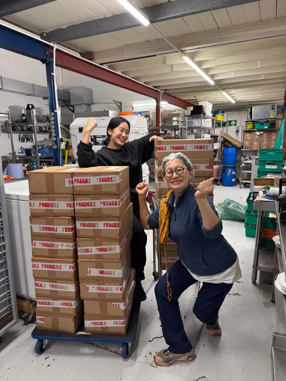 Xien and Jolene celebrating between stacks of freshly packed Mama Yu boxes
