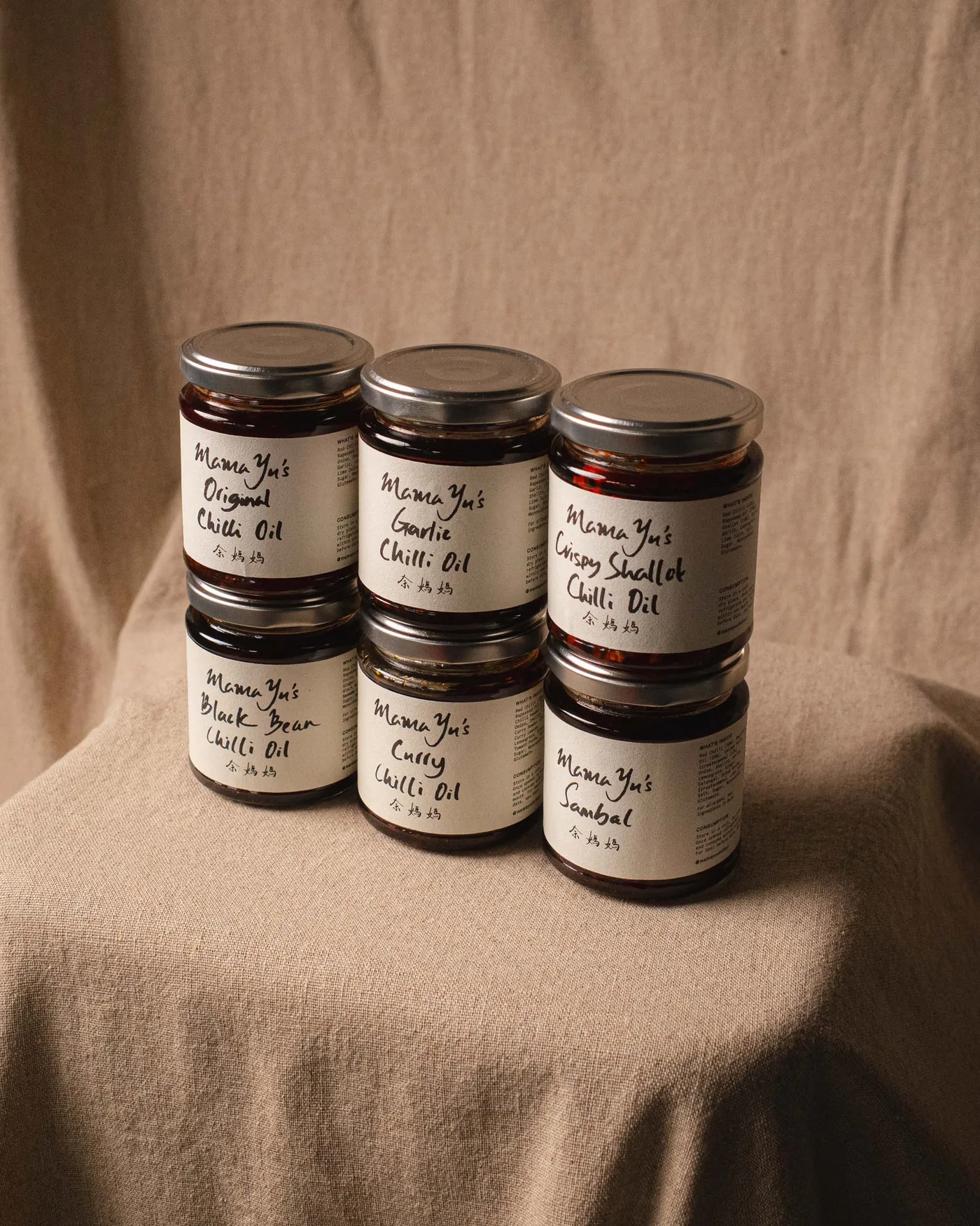 The full Mama Yu range of chilli oils and sambal stacked on warm linen